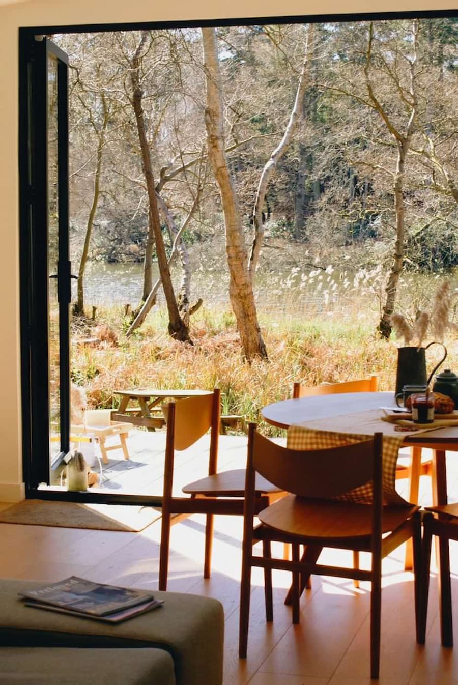 Koto cabin dining room with bi-fold doors across the whole width of the wall which are open overlooking the woodland and lake