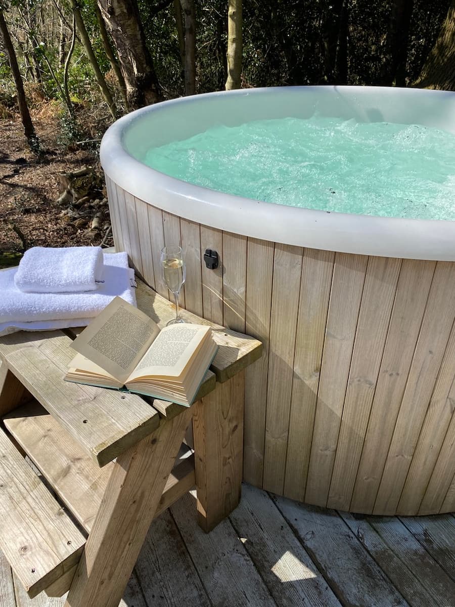 Hot tub with steps leading up to it, styled with white towels, a glass of Prosecco and an open book