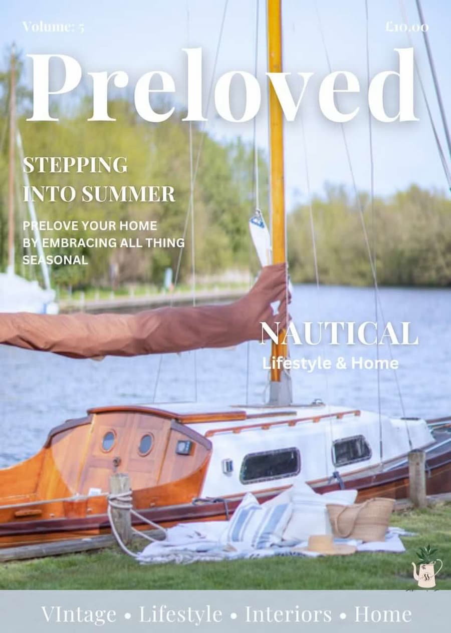 Front cover of the summer edition of the Preloved magazine. Preloved in white large font at the top of the page Picture of a sail boat moored up on an embankment. In front of the boat is a styled set up with a pale blue and white chequered blanket, blue and white striped cushions and a straw hat and bag positioned to the right. Pale Blue banner to the bottom of the page with Vintage, Lifestyle, Interiors, Home written across the centre
