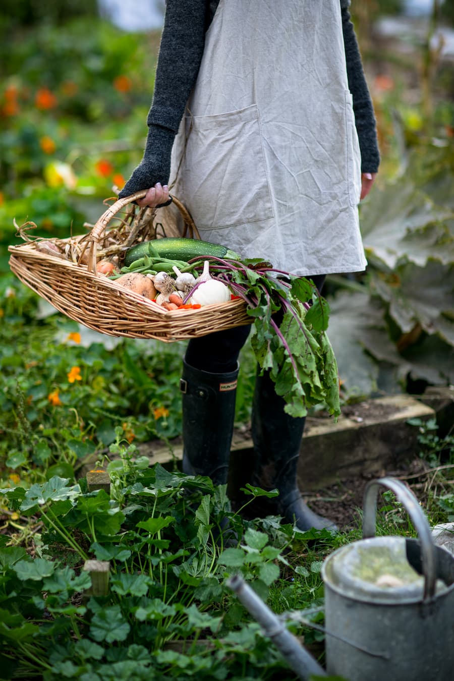Woman with a linen apron holding a straw basket full of home-grown vegetables