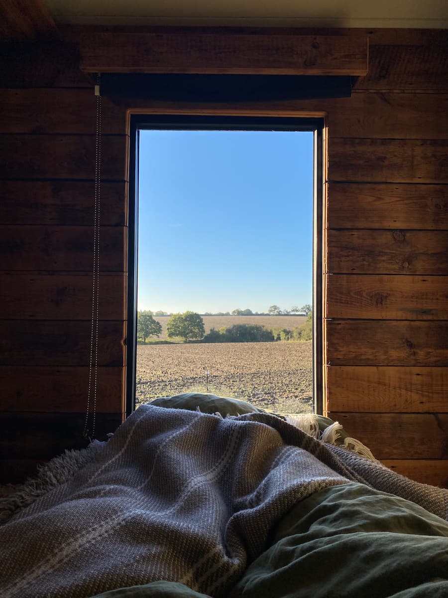 View from the bedroom of the shepherds hut overlooking farmland and a bright blue sky