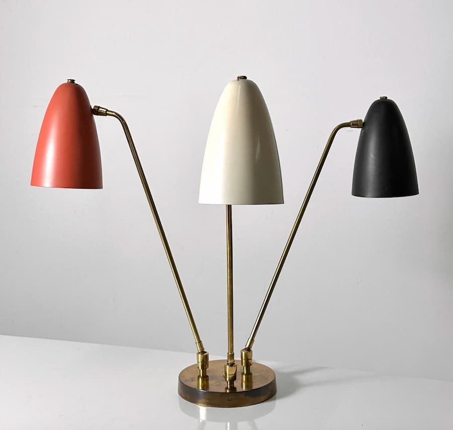 Three arm articulated table lamp with rust orange, cream and black shades and brass base
