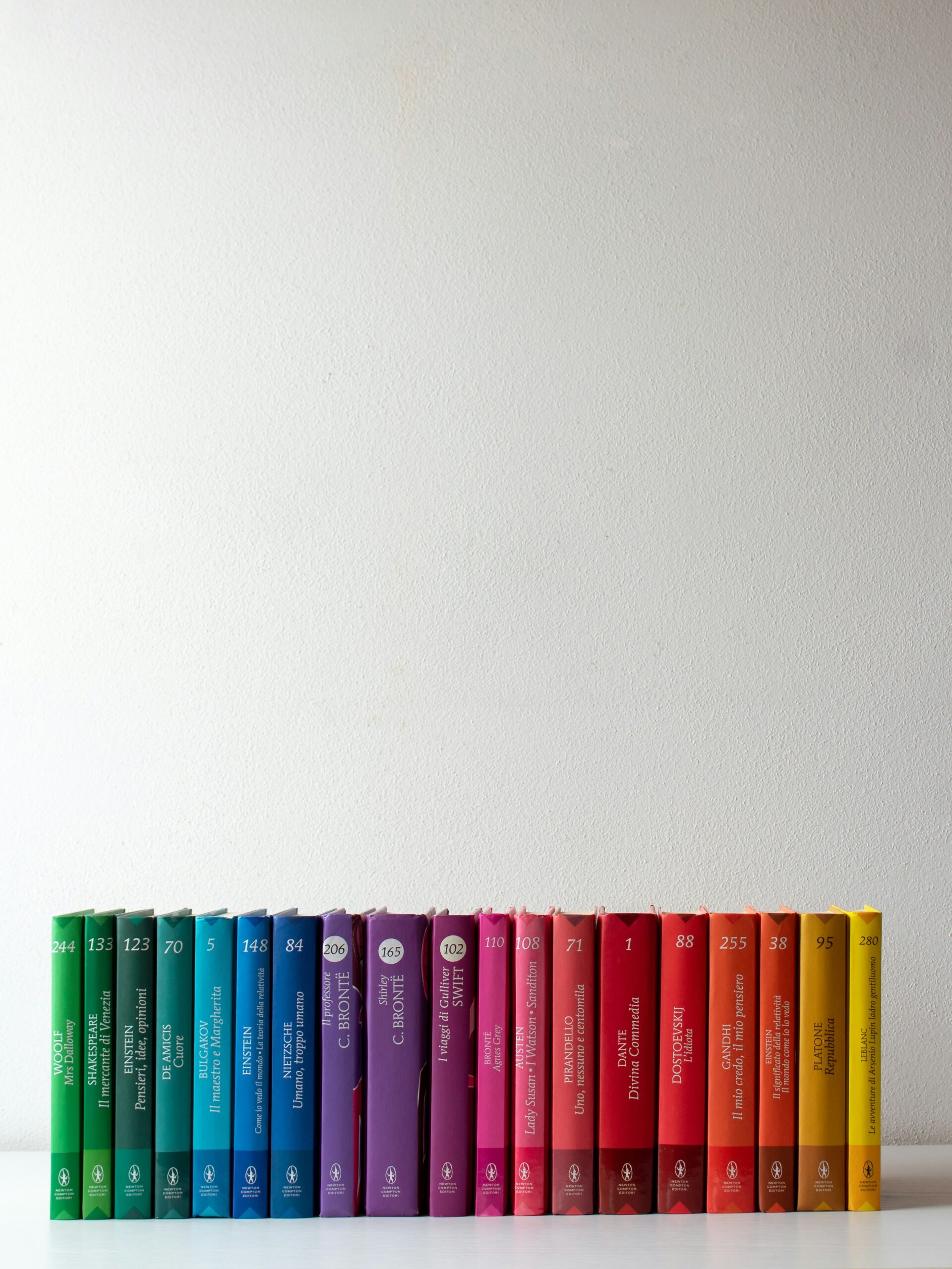 Row of books in the colour theme of a rainbow, starting from the left with green, into blue, purply, pink, red, orange and finishing with yellow
