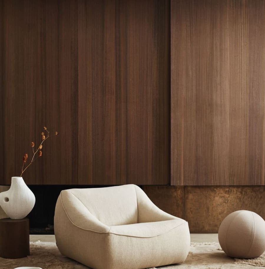 white single chair positioned in front of a large dark wood panelled feature wall