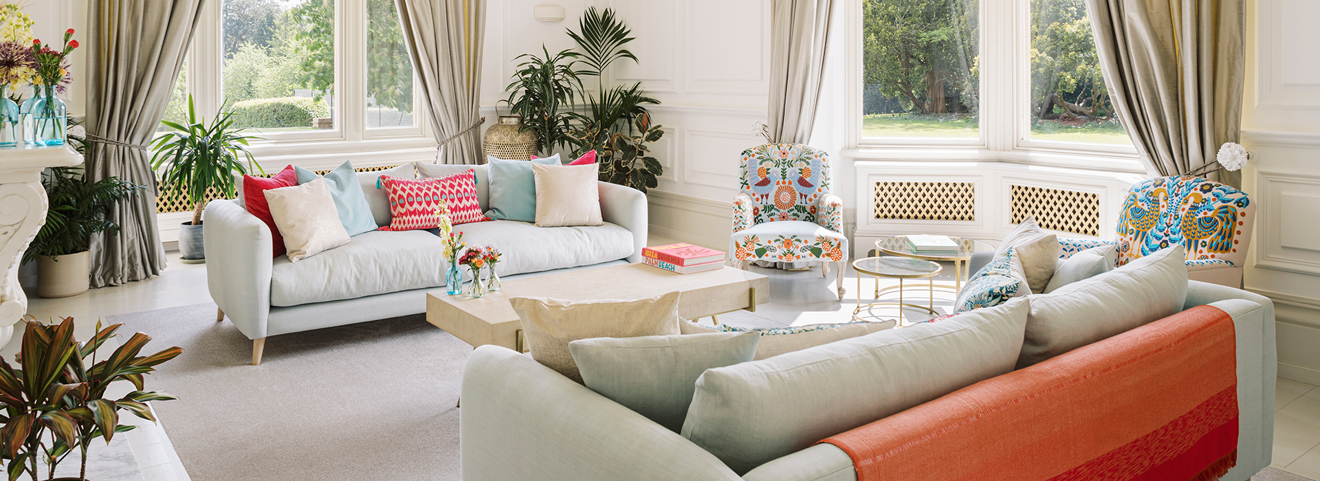 Large bright lounge with two cream sofas positioned opposite each other covered in brightly coloured cushions of turquoise and cerise pink