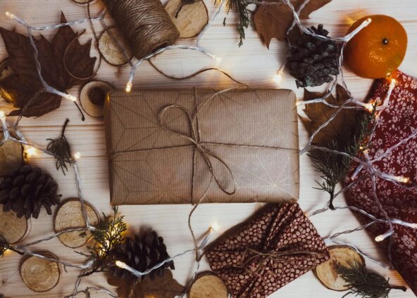 Flat lay of a gift wrapped in brown paper and autumnal accessories and Christmas lights placed around the edge