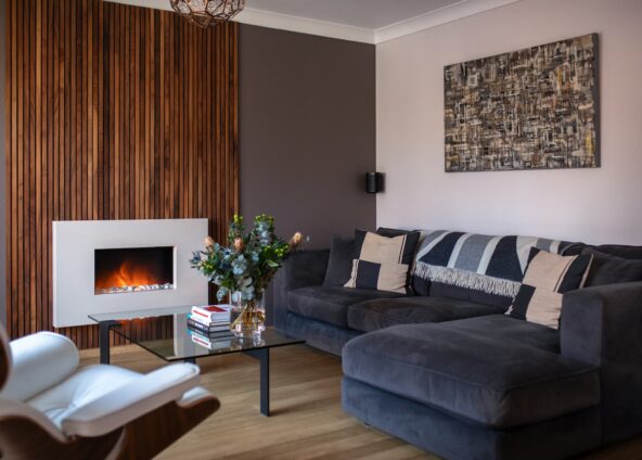 Interior design trends 2024 Modern living room with walnut feature wall and marble electric fire positioned in the centre with grey corner sofa and modern glass coffee table following one of the interior design trends for 2024